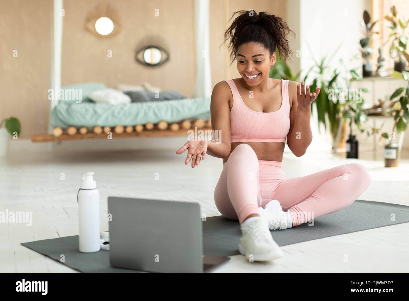 Online exercise session marathon. Happy black woman sitting on floor mat and talking with coach, exercising at home Stock Photo