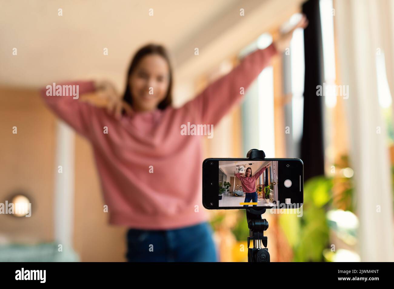 Modern content creator. Excited teen girl filming video blog for social network, using cellphone on tripod to broadcast Stock Photo