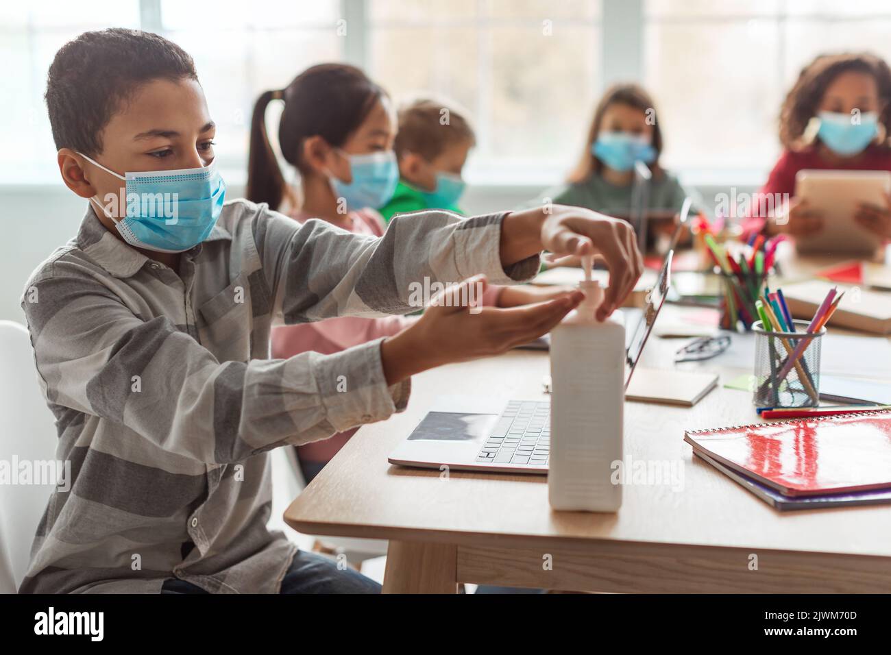 African American Schoolboy Using Sanitizer Disinfecting Hands In Classroom Stock Photo