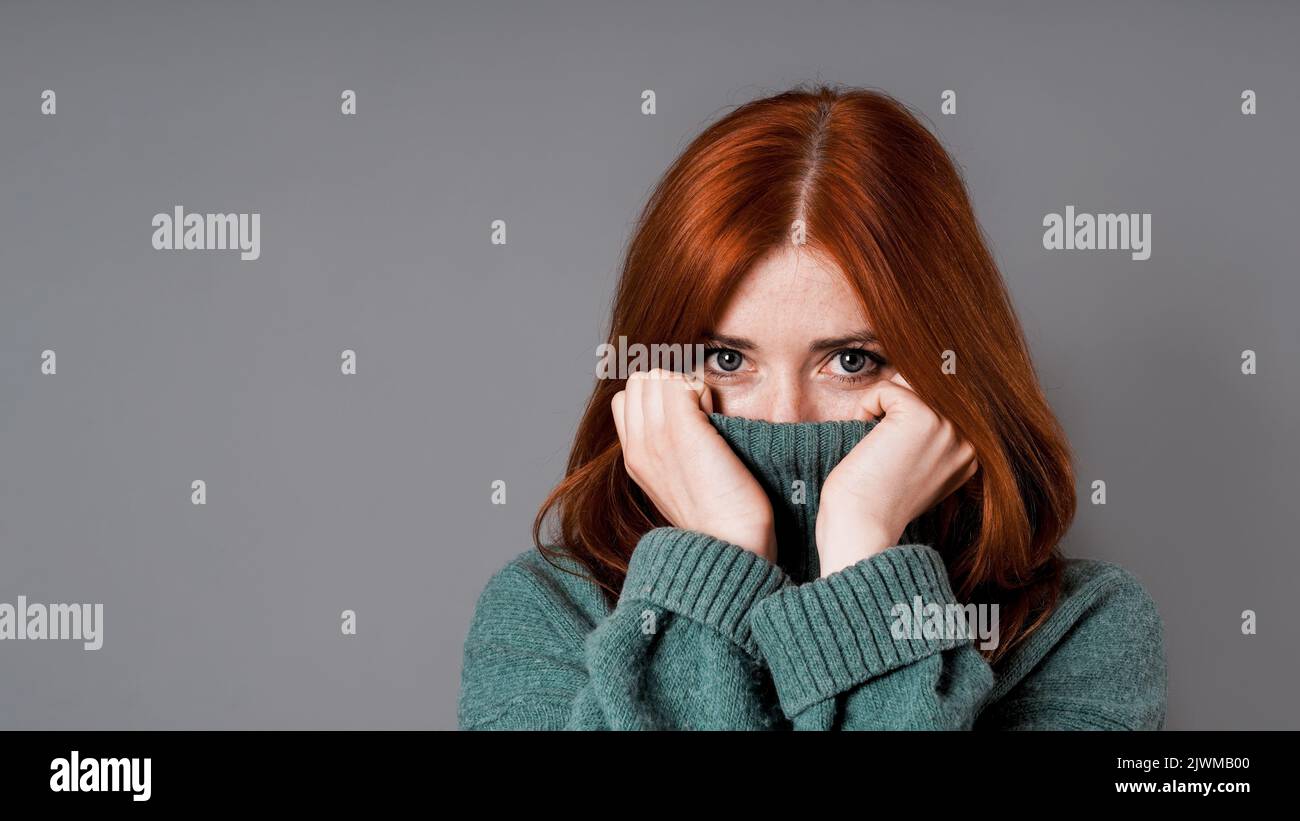 shy or embarrassed woman pulling turtleneck sweater over face Stock Photo