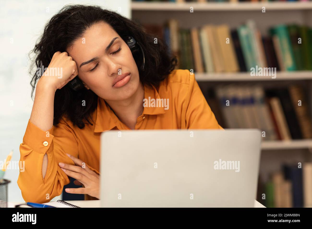 Tired mixed race female student sleeping on table in front of laptop computer, preparing for exams in library Stock Photo
