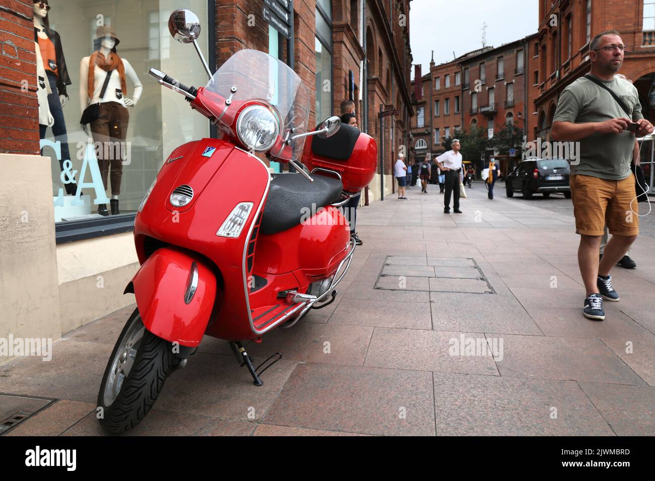 TOULOUSE, FRANCE SEPTEMBER 28, 2021 People walk by red Piaggio Vespa