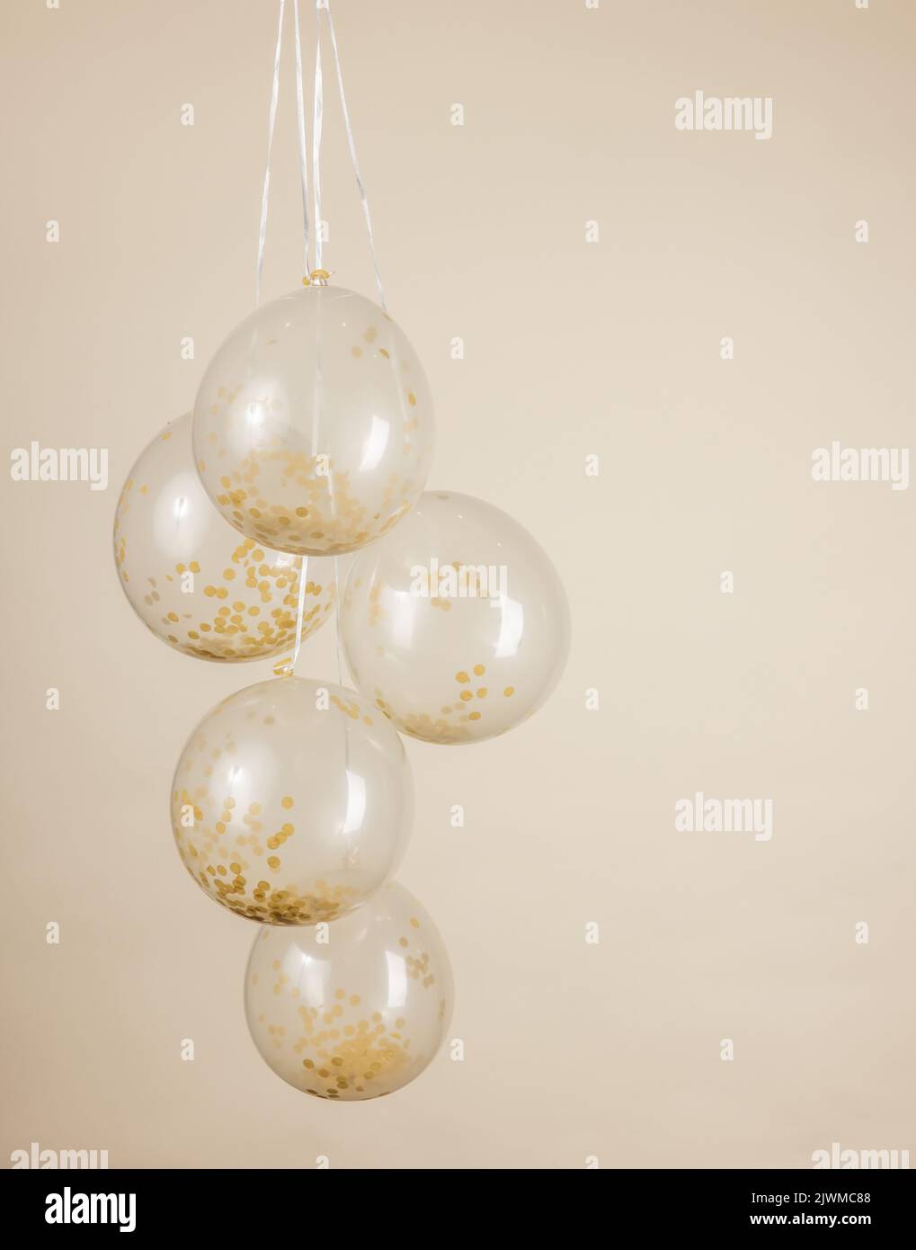 A monochromatic gold and cream confetti clear balloons against a light creamy yellow backdrop with copy space. Stock Photo
