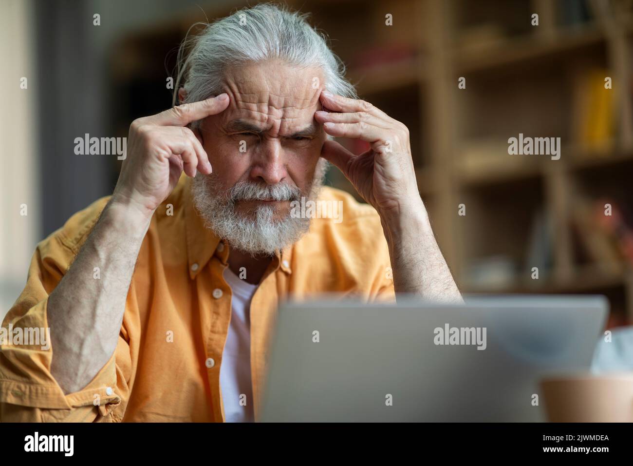 Stressed senior man working from home, using laptop Stock Photo