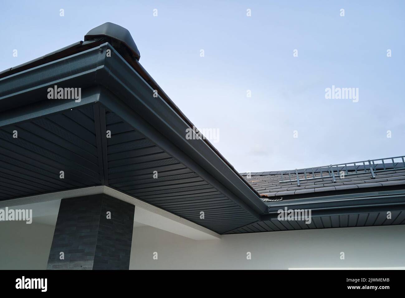 House corner with brown metal planks siding and roof with steel gutter rain system. Roofing, construction, drainage pipes installation Stock Photo