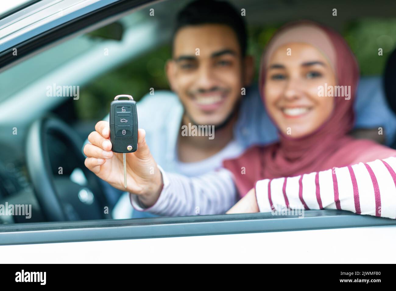 Dreams come true. Glad happy young arab husband and wife in hijab customers show keys at new car, close up Stock Photo