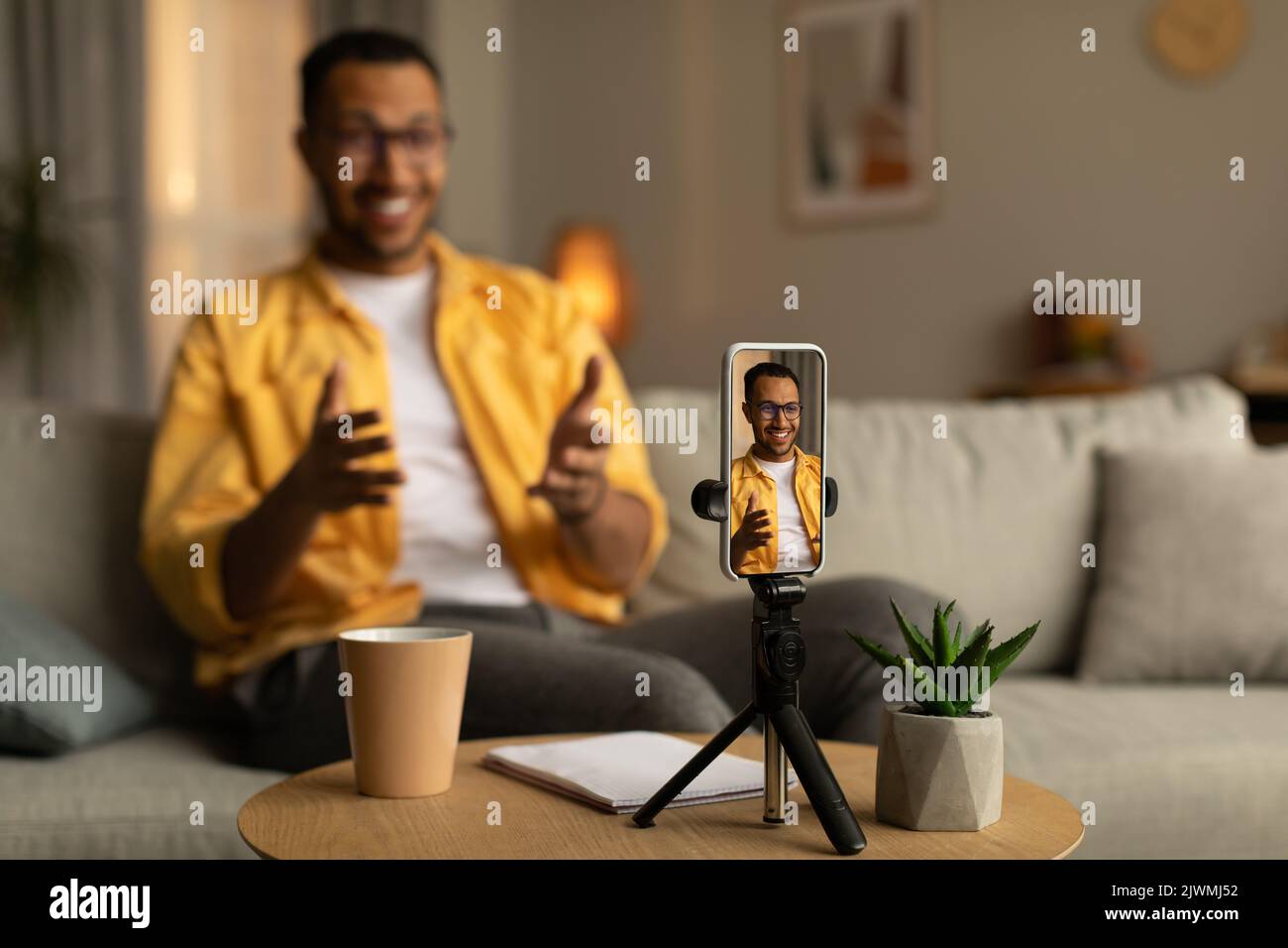 Happy young black teacher giving online lecture, using smartphone to communicate with students from home Stock Photo