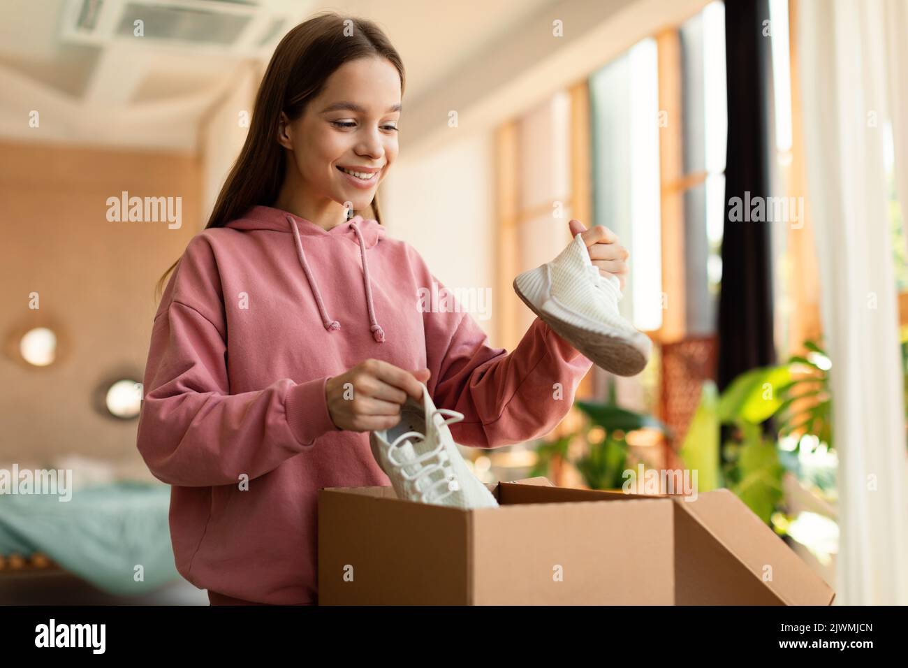 Shopping and delivery concept. Happy customer girl holding new sneakers, unpacking cardboard box