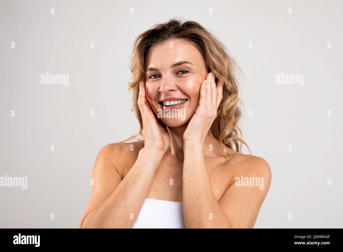 Antiage Skincare. Attractive Middle Aged Female Touching Face And Smiling At Camera Stock Photo