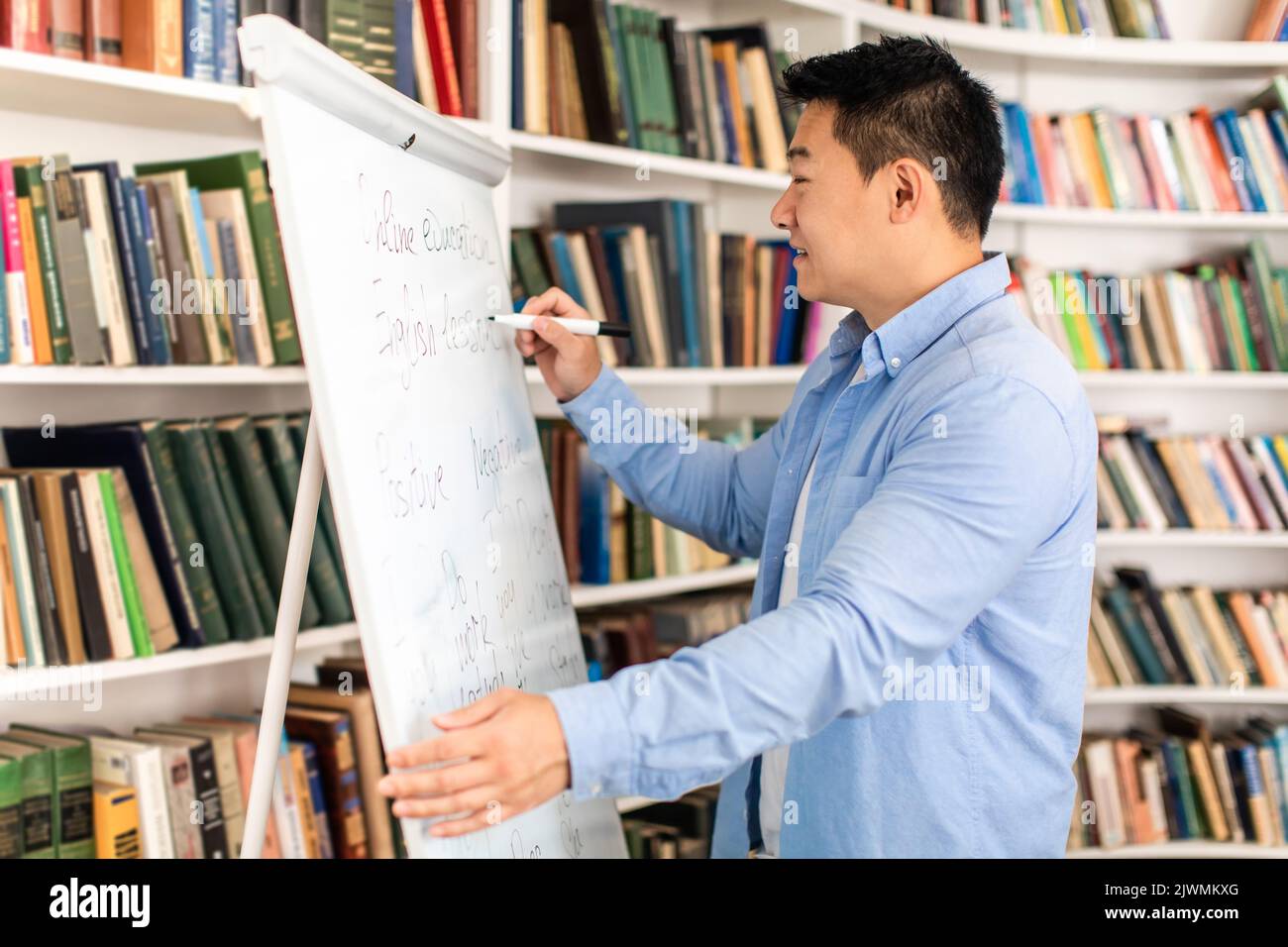 Chinese Teacher Man Writing On Whiteboard Standing In Modern Classroom Stock Photo