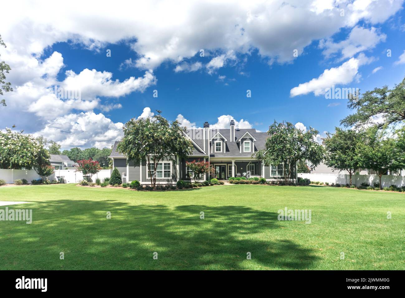 The side view of the backyard of a large gray craftsman new construction house with a landscaped yard. Stock Photo