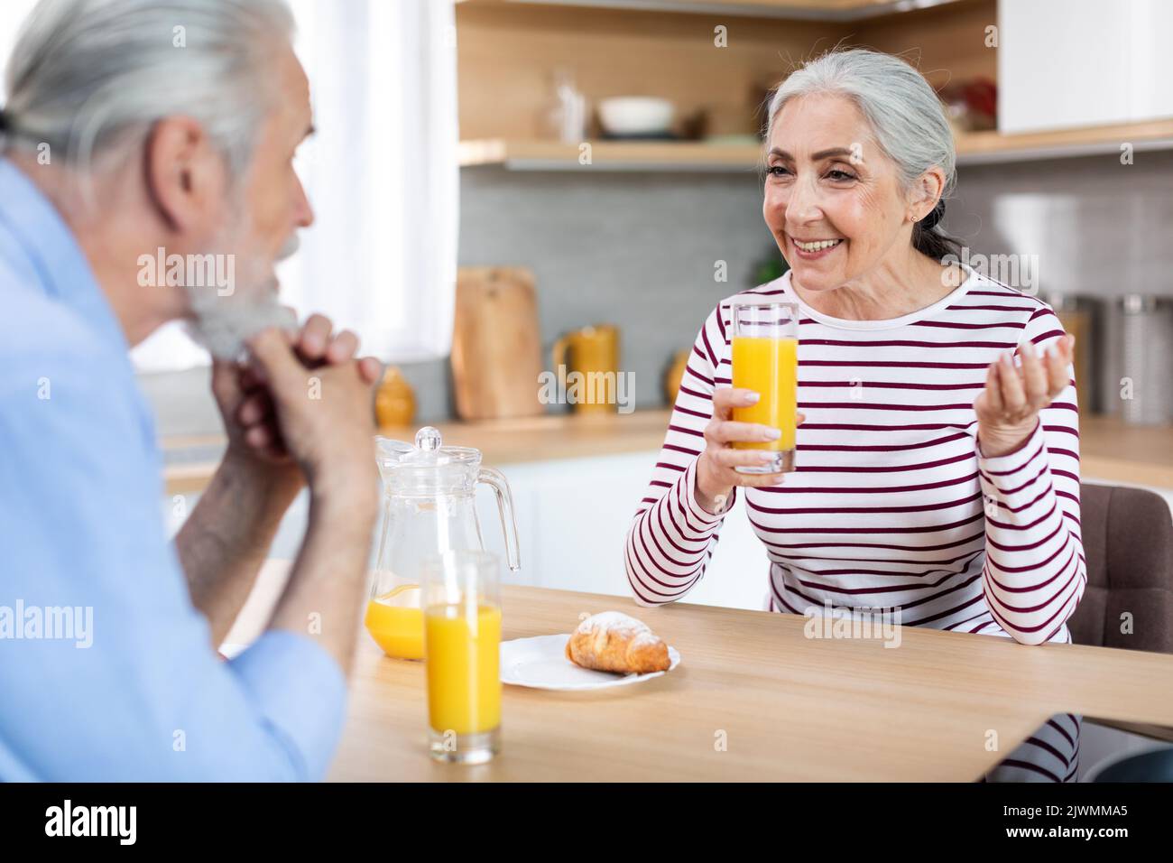 Happy Senior Spouses Chatting While Having Breakfast In Kitchen Together Stock Photo
