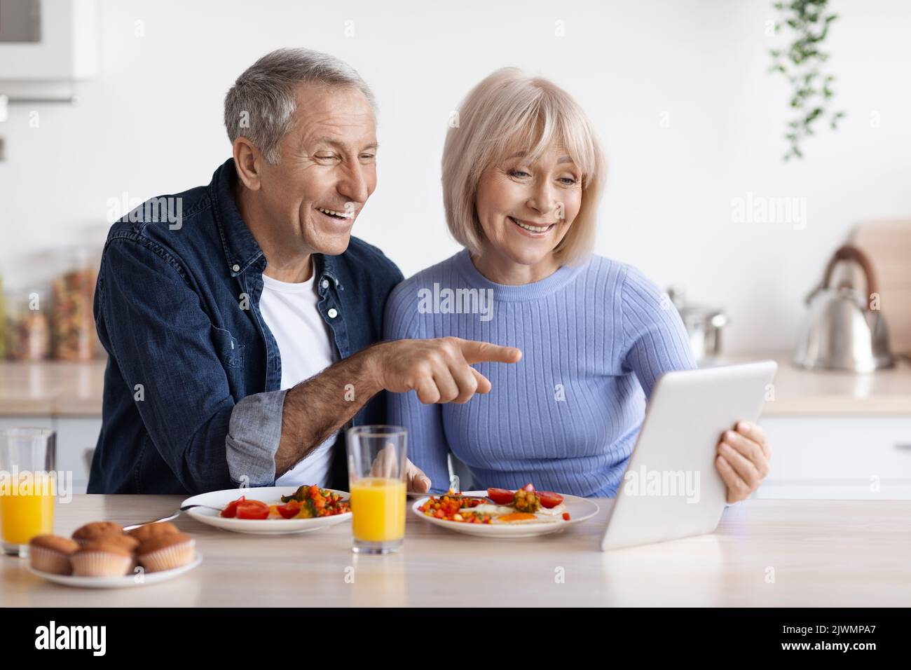 Cheerful elderly couple using digital tablet while having breakfast Stock Photo