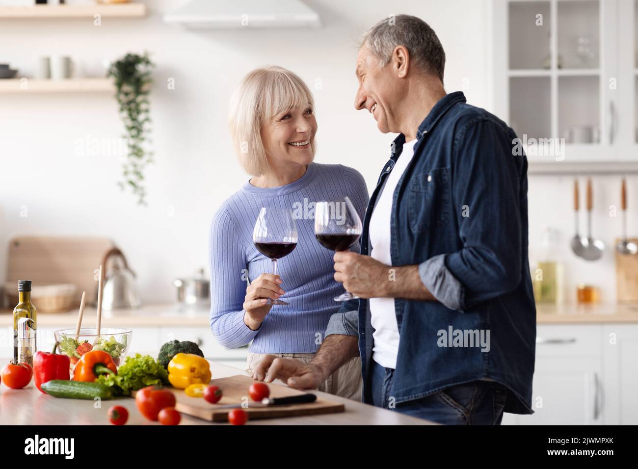 Positive elderly spouses drinking red wine while preparing meal Stock Photo