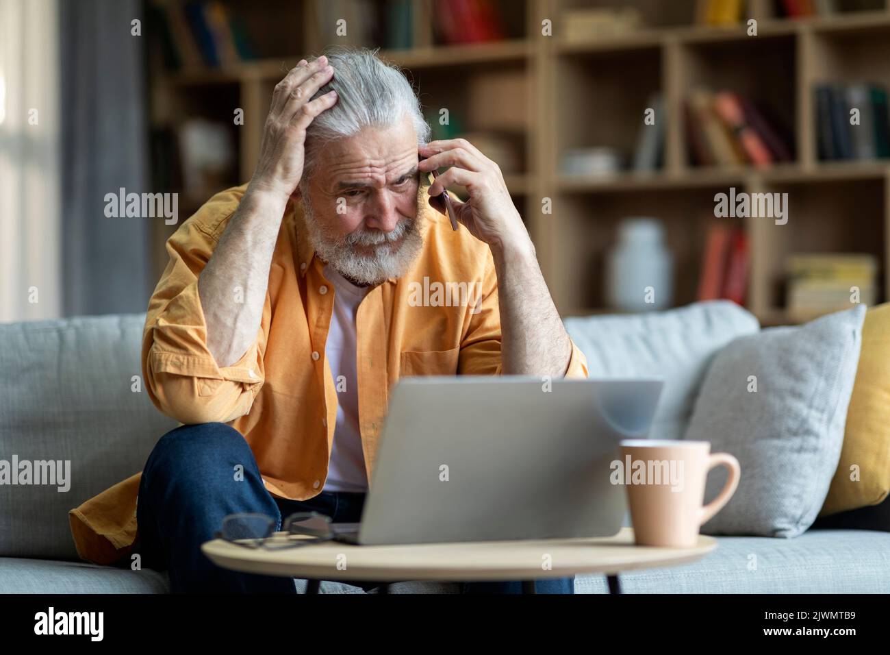 Upset elderly man using laptop, having phone conversation Stock Photo
