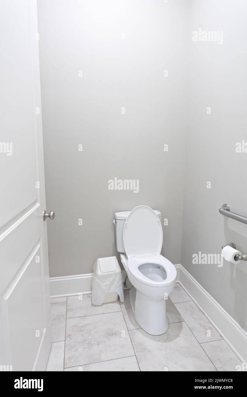 A small half bathroom with gray walls and a toilet with tile floors in a new construction house with a handicap railing. Stock Photo