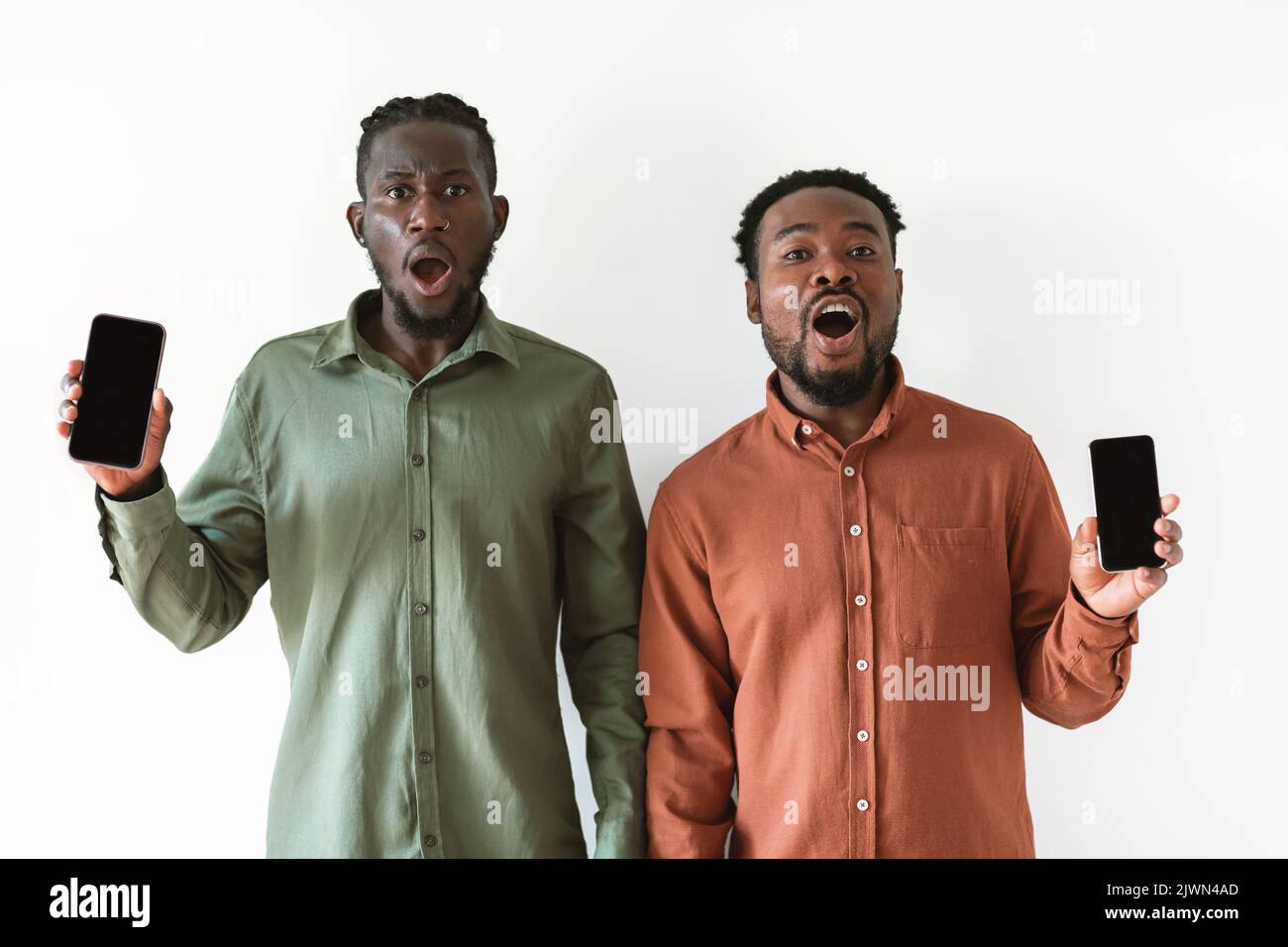 Two Shocked African Guys Showing Smartphone Screens Over White Background Stock Photo