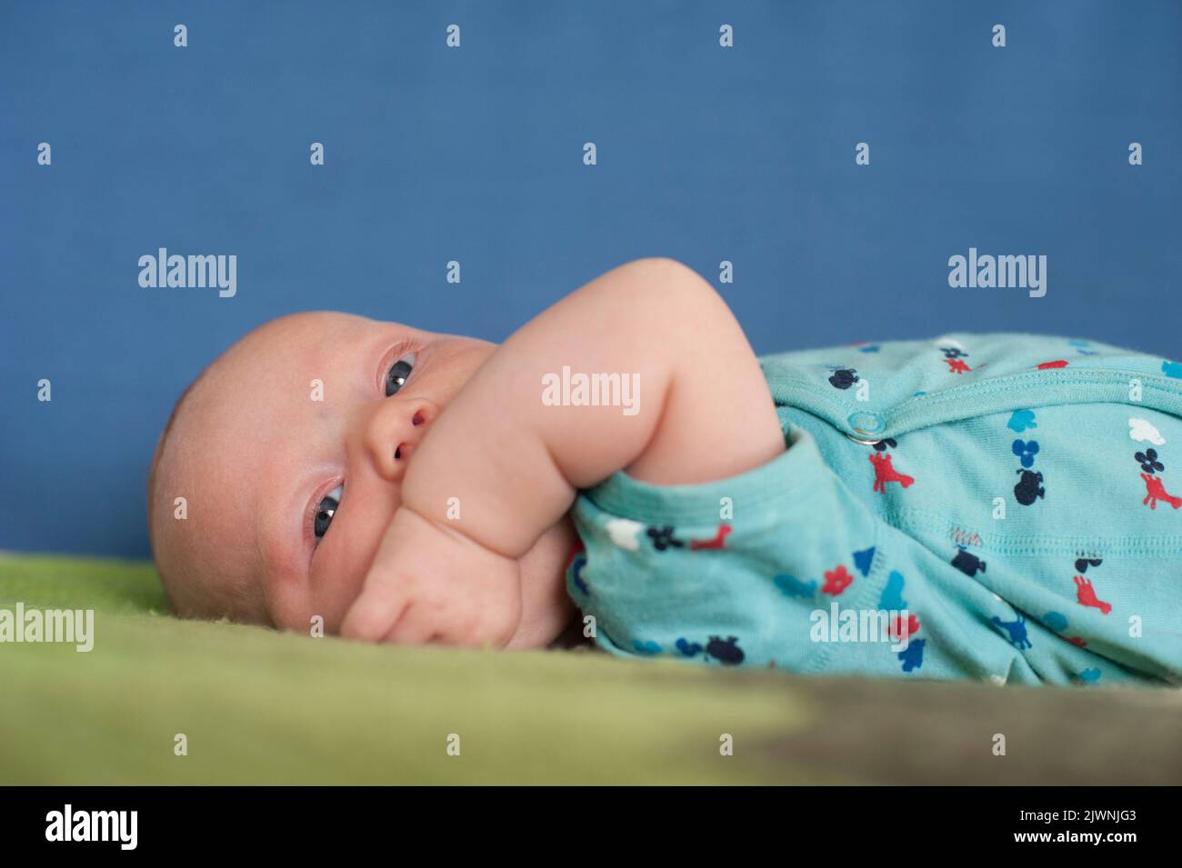 A portrait of a three-month-old baby on a crocheted blanket chews on her wrist. Stock Photo