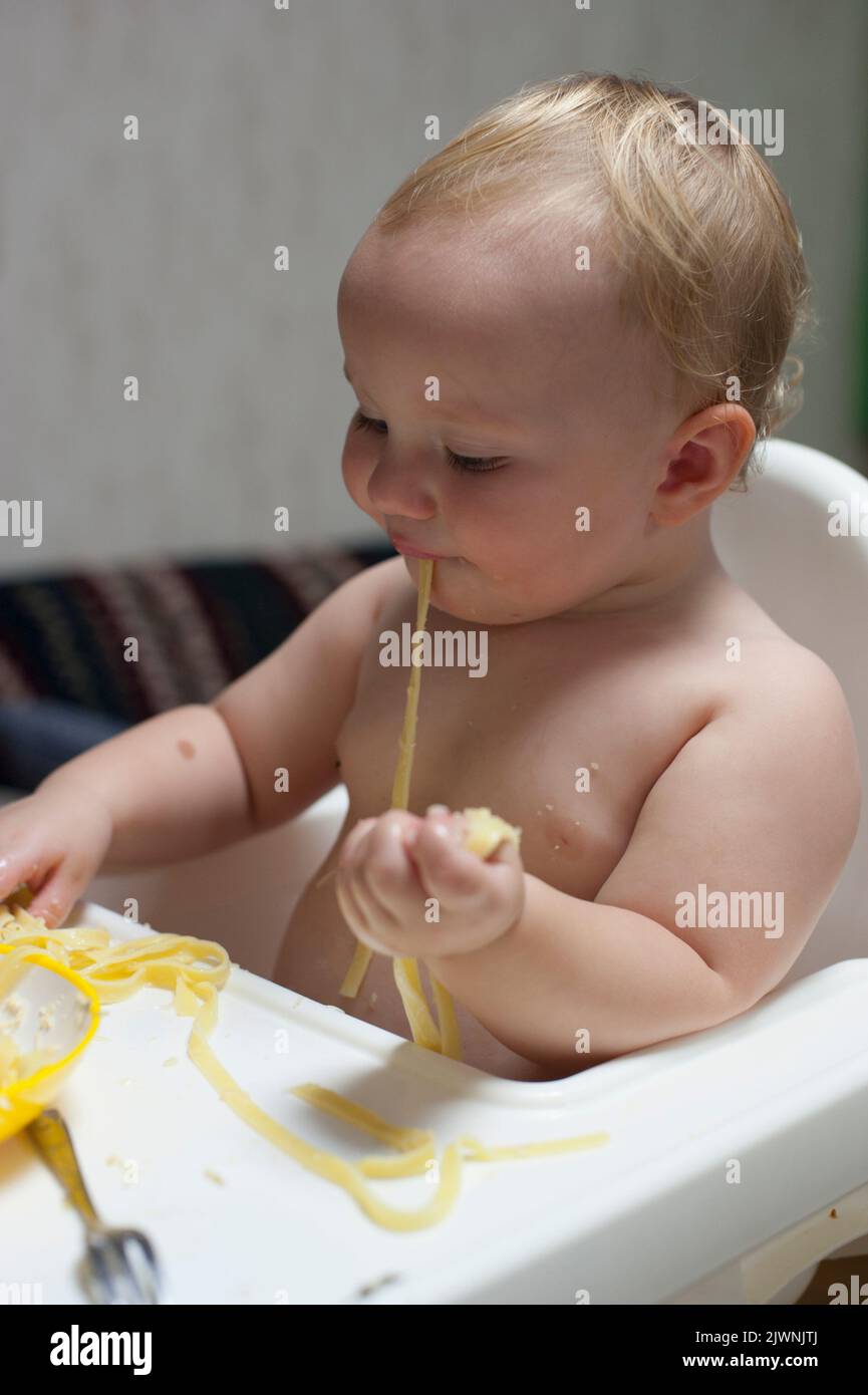A toddler discards her fork and eats a meal of long spaghetti noodles using her hands. Stock Photo