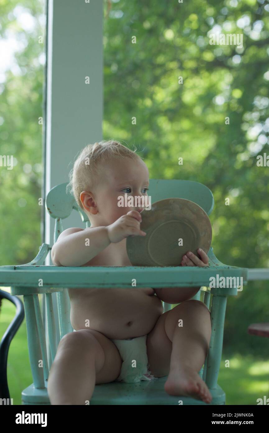 A toddler in an old-fashioned highchair holds up her empty plate. Stock Photo