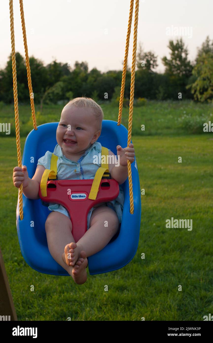 A toddler enjoys a baby swing in the summer. Stock Photo