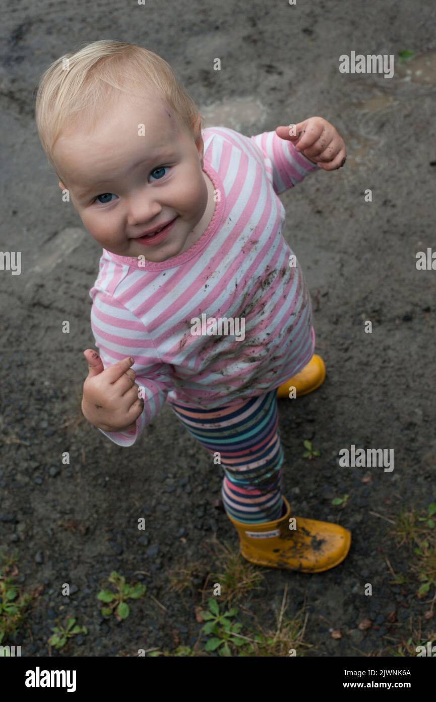 A toddler in rain boots explores a muddy puddle and gets dirty. Stock Photo