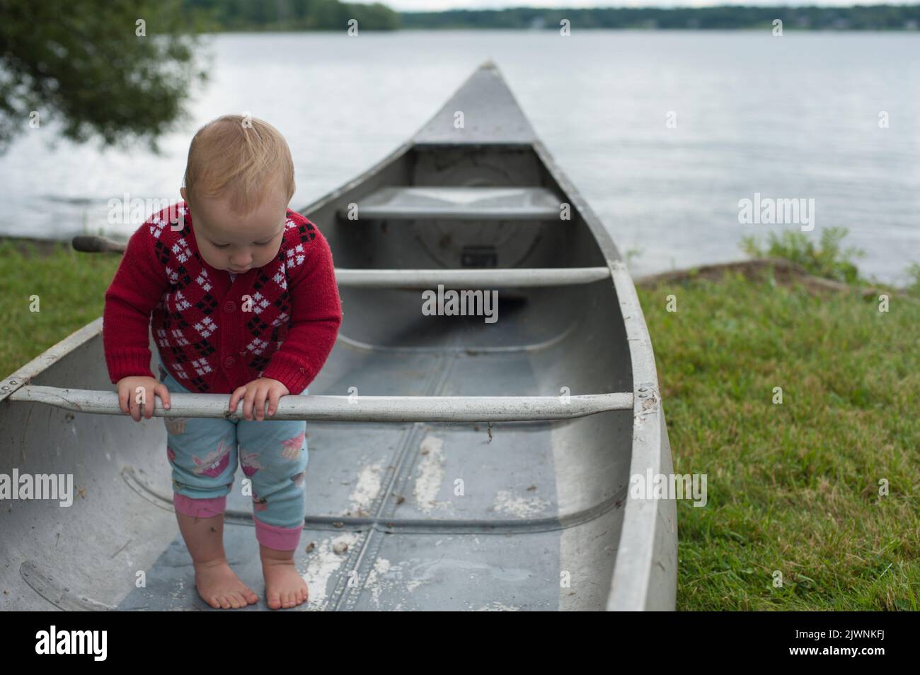 A toddler explores a grumman canoe on the banks of the Saint Lawerence River. Stock Photo