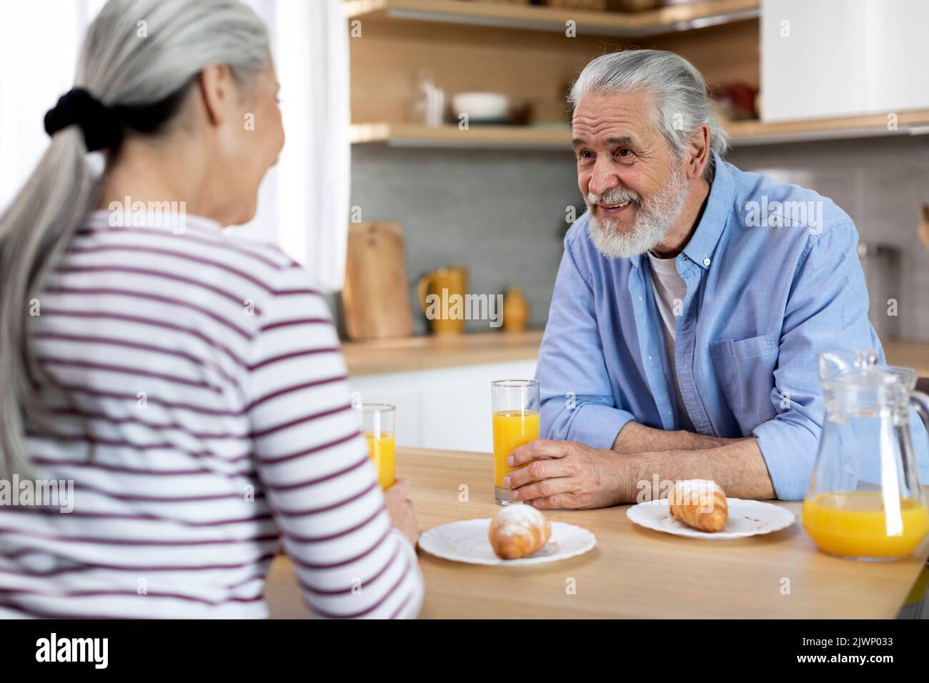 Senior Married Couple Chatting While Having Breakfast Together In Kitchen Stock Photo