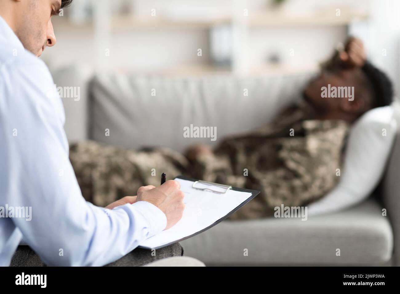 Psychotherapist taking notes while having conversation with veteran Stock Photo