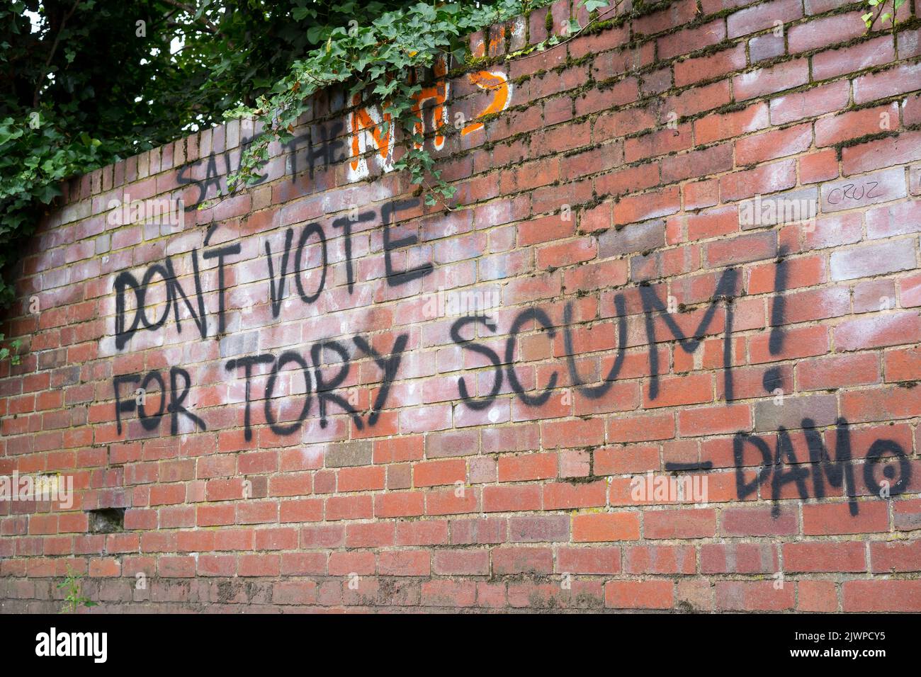 Graffiti words written on an outdoor UK brick wall: 'Save the NHS & Don't Vote for Tory Scum!' Anti-conservative opinion. Stock Photo