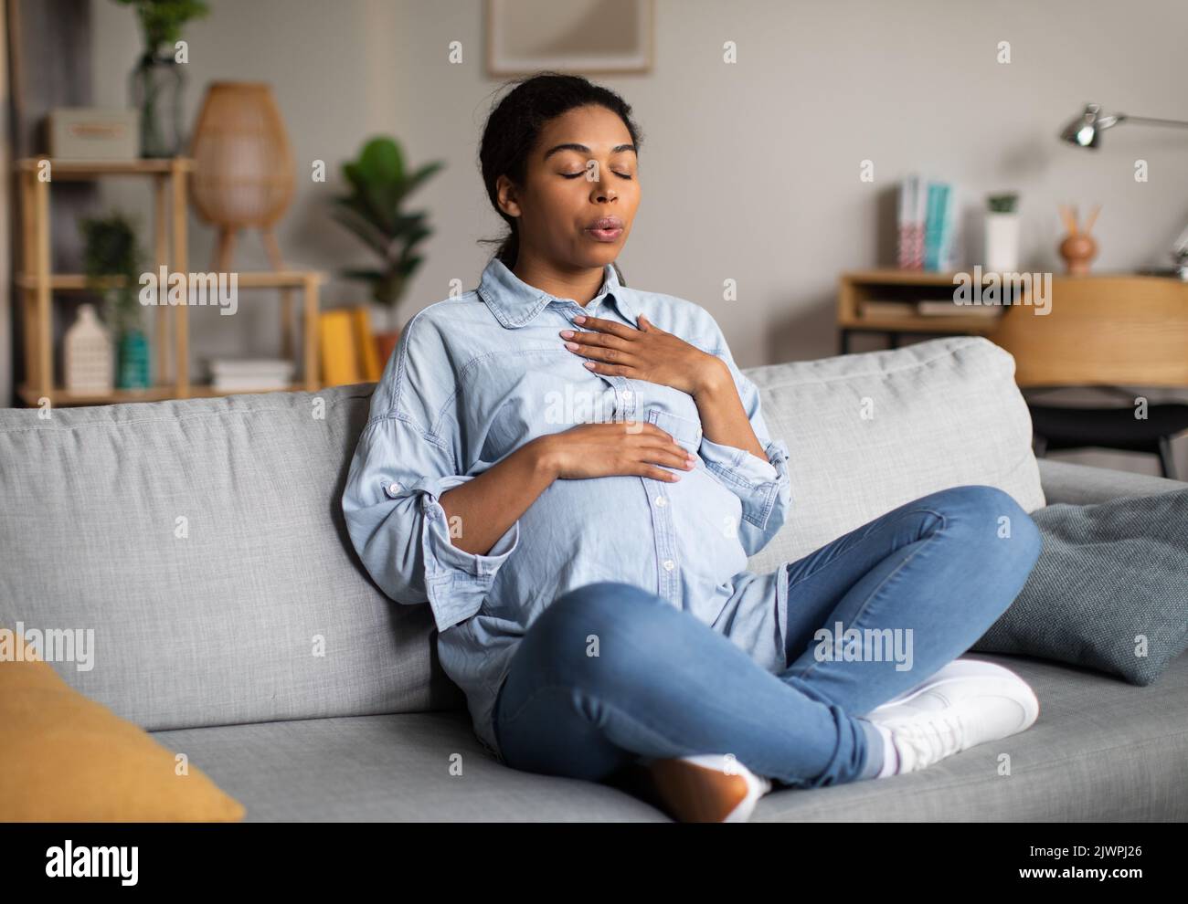 Pregnant African American Woman Doing Breathing Exercise Sitting At Home Stock Photo