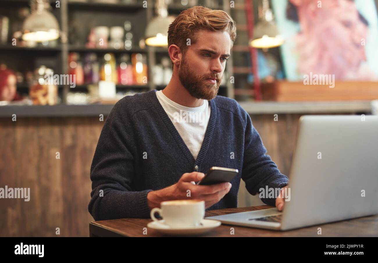 Down at the cafe for a bit of blogging. a young man using a laptop and phone in a cafe. Stock Photo