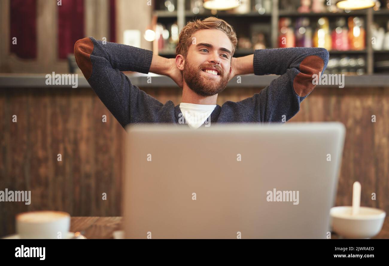 Enjoying the perks of being a freelancer. a relaxed young man using a laptop in a cafe. Stock Photo