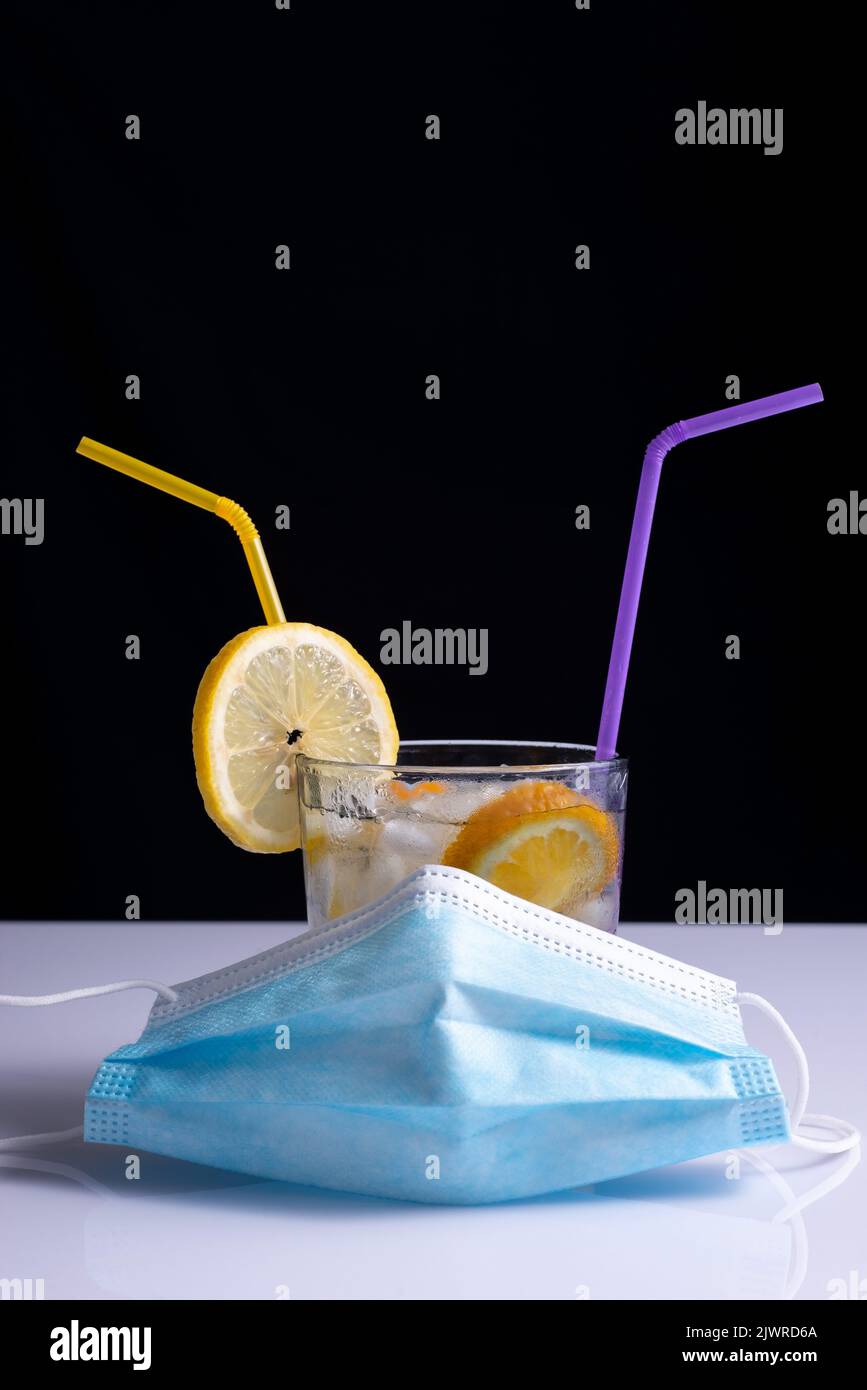 fruity coronavirus cocktail in protective mask concept on white table and black background. Stock Photo