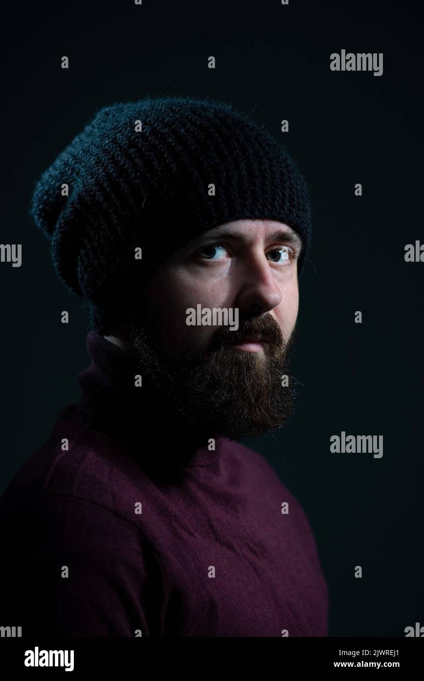 dramatic portrait of millennial in black knitted hat and sweater on dark background. Stock Photo