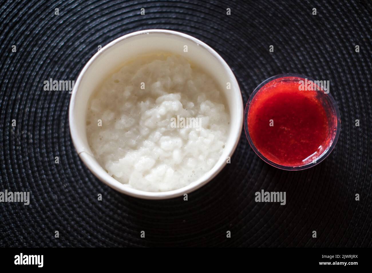 Rice flake porridge in a white round carton take-away box with fresh strawberry jam. Stock Photo