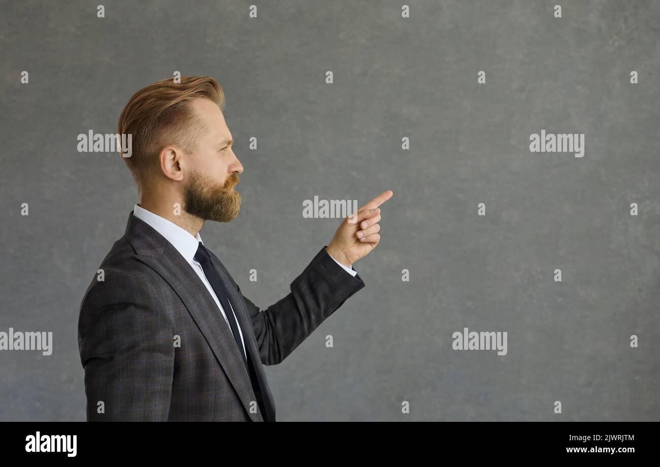 Side view of businessman pointing at copy space standing isolated on grey background Stock Photo
