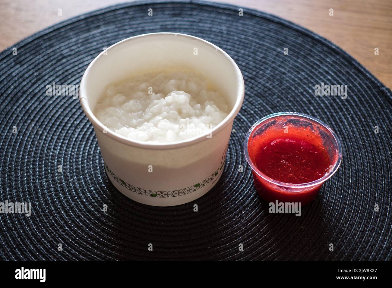 Rice flake porridge in a white round carton take-away box with fresh strawberry jam. Stock Photo