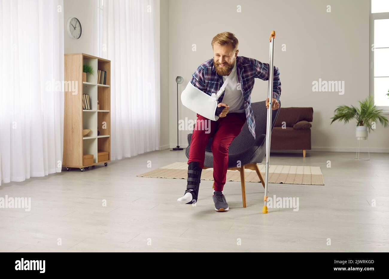 Man with broken leg and arm tries to get up from chair and walk with