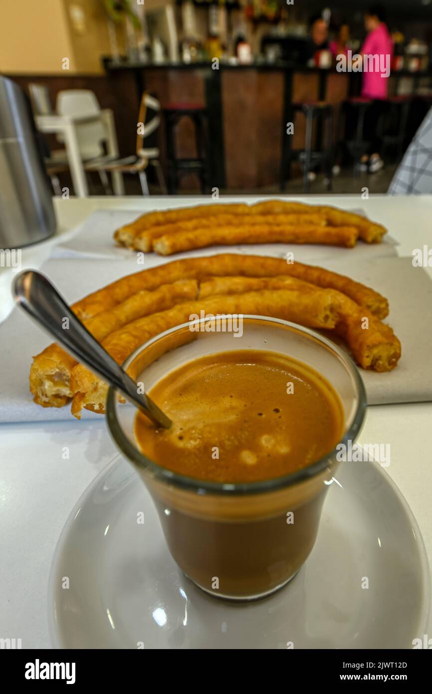 Glass of coffee with milk with churros in a cafeteria. Stock Photo