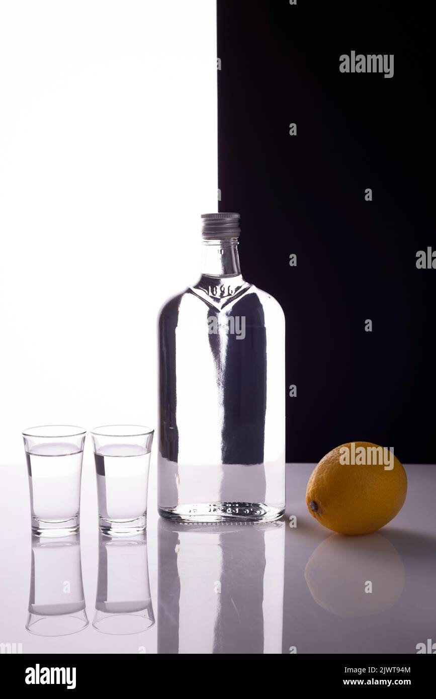 gin bottle with shot glasses on black and white background alcoholic drink with lemon Stock Photo