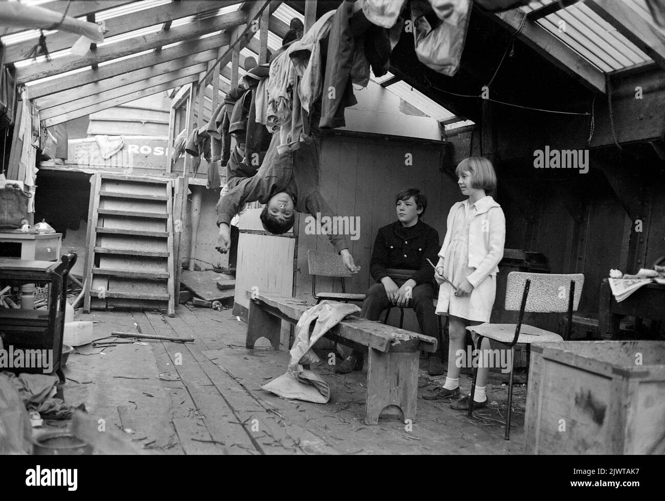 London, England, circa 1967. A group of children of The Pirate Club aboard ‘Rosedale’, a disused barge which served as their clubhouse. Two boys are dangling upside-down from a roof beam while another boy and girl look on. Used nails and other litter have been discarded on the deck of the barge, left from its restoration work. The Pirate Club, a children’s boating club was formed in 1966 at Gilbey’s Wharf on the Regent’s Canal near Camden, London. A number of small boats and canoes had been donated for the children’s use. Stock Photo
