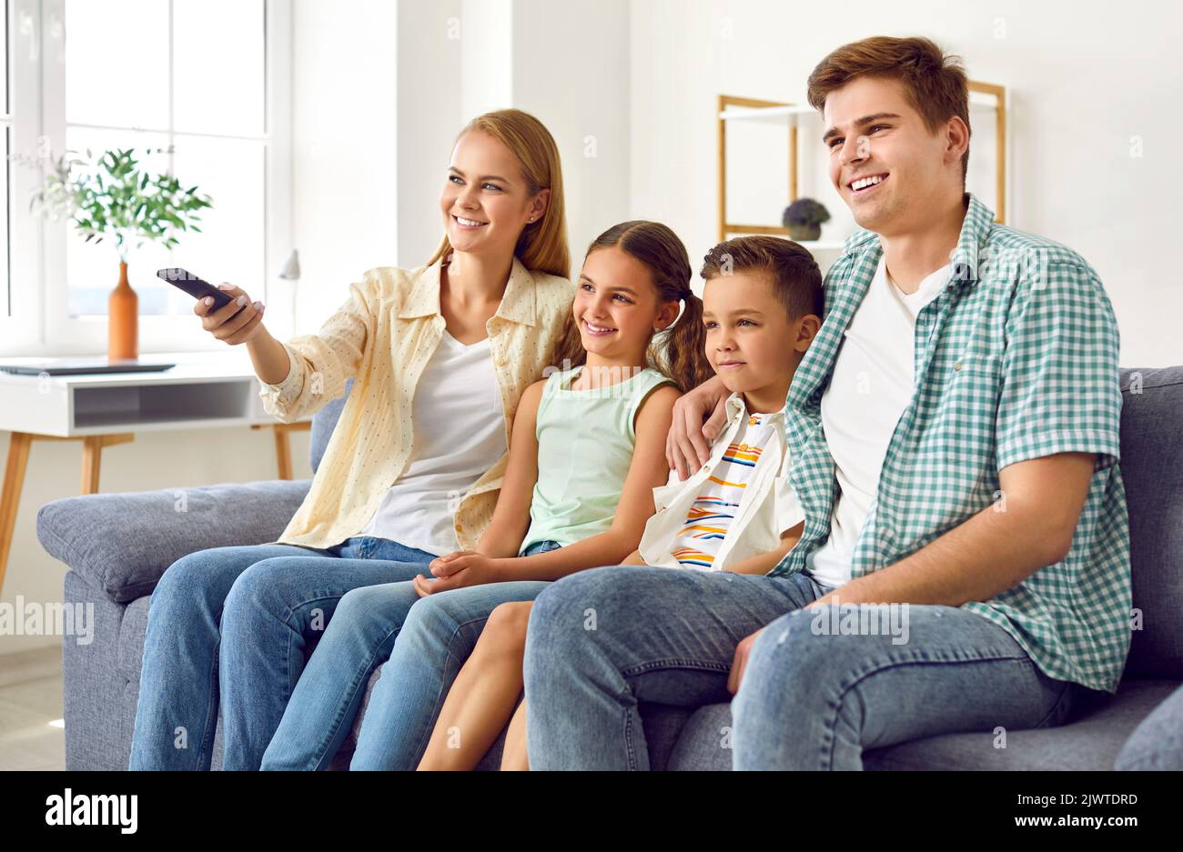 Happy parents and children sitting on the couch and watching television together Stock Photo