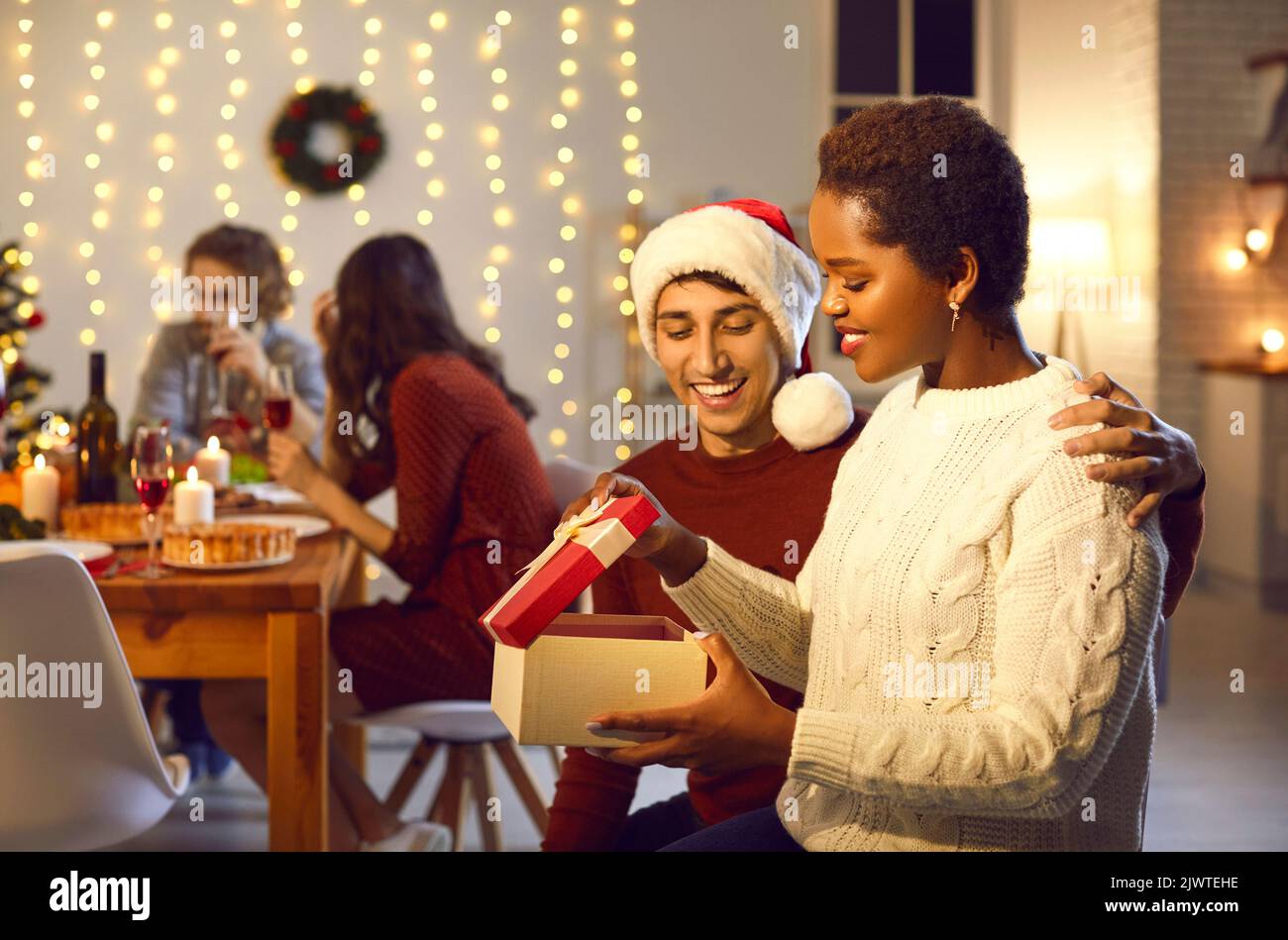 Man surprises his beloved woman by giving her present during family Christmas dinner. Stock Photo