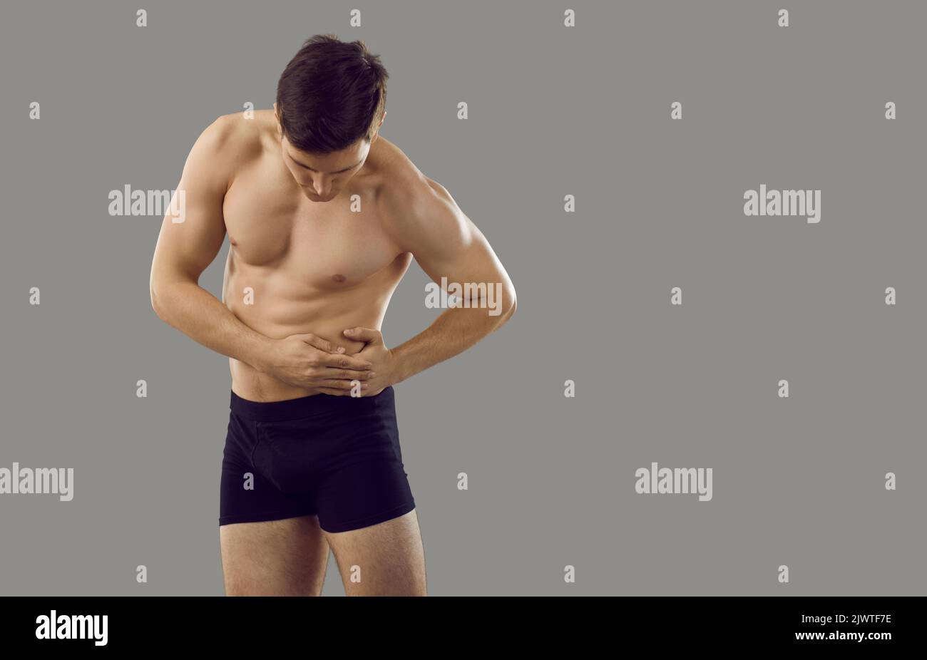 Young man touching left side of abdomen feeling severe pain standing on gray background. Stock Photo