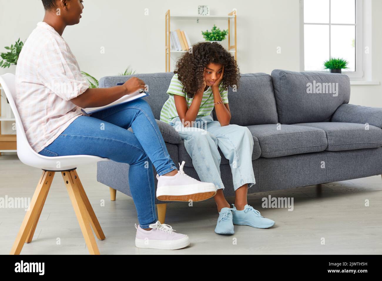 Upset African American girl teenager sits on couch in office of school psychologist and looking down Stock Photo