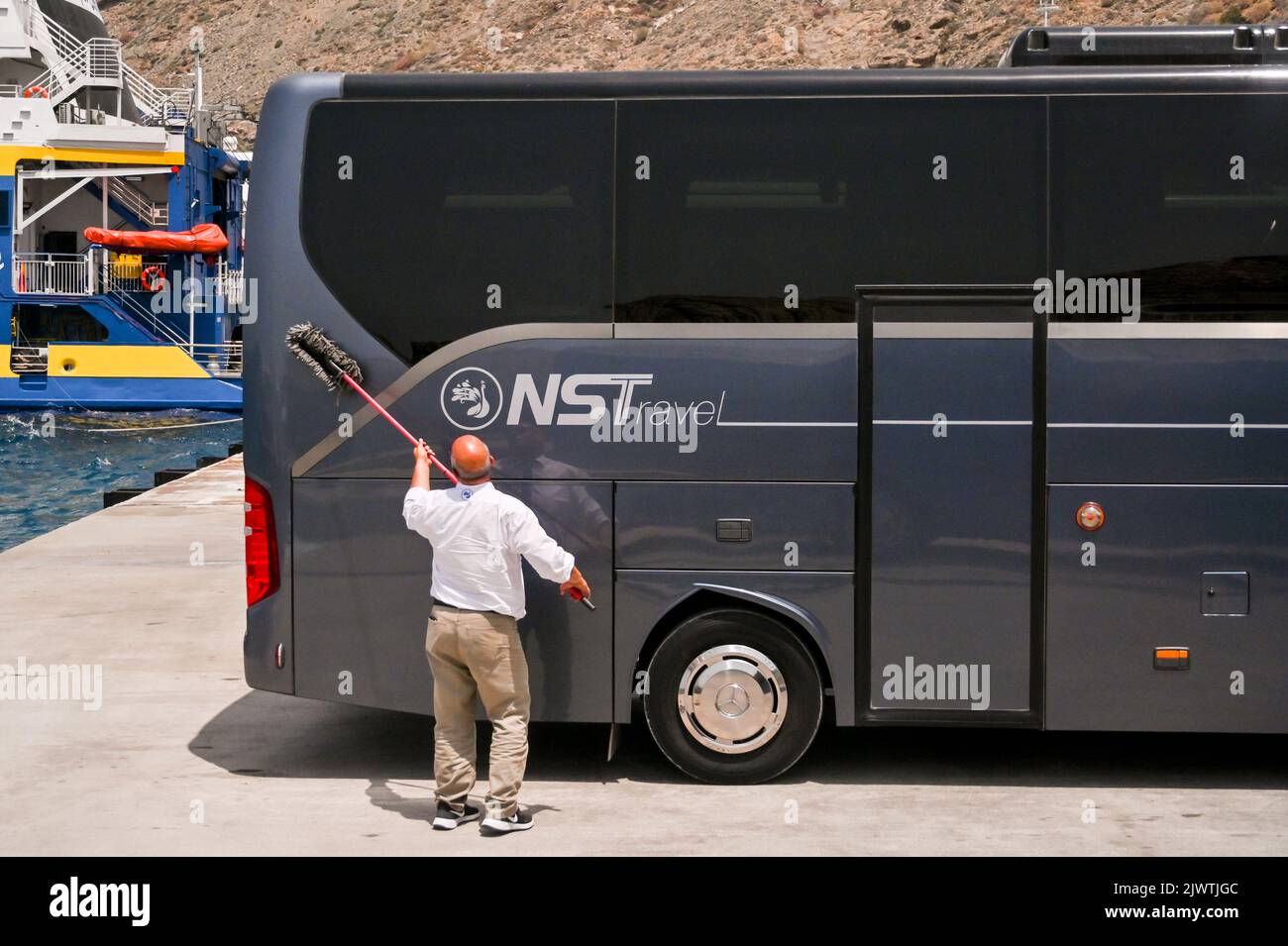 Santorini, Greece - June 2022: Coach driver washing the side of a modern bus before picking up tourists Stock Photo