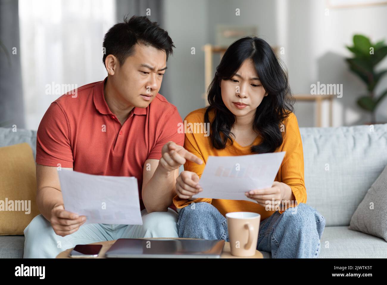 Confused asian spouses checking bills, home interior Stock Photo
