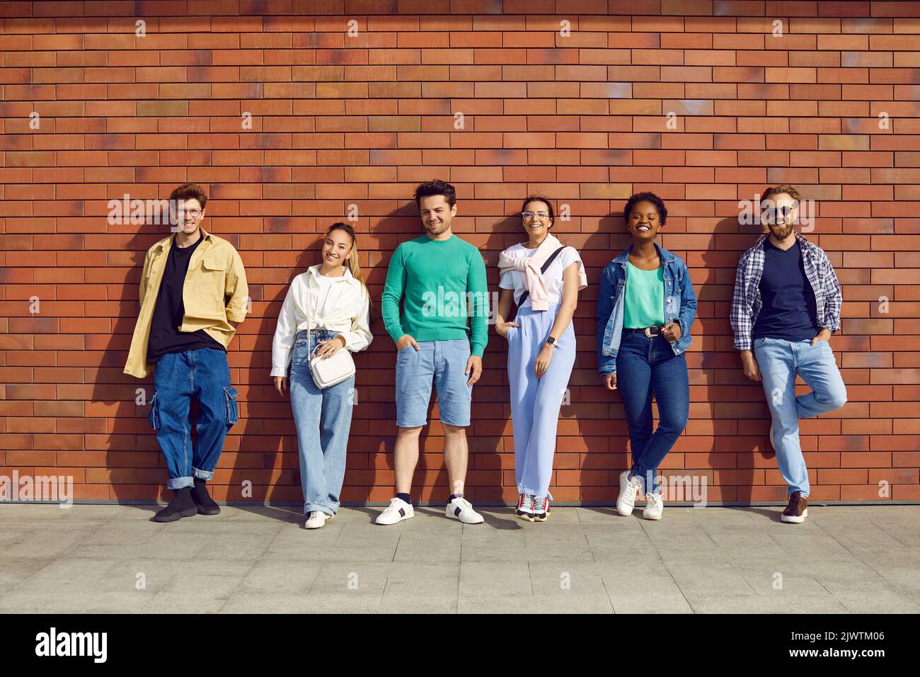 Stylish different young people stand in row and pose against background