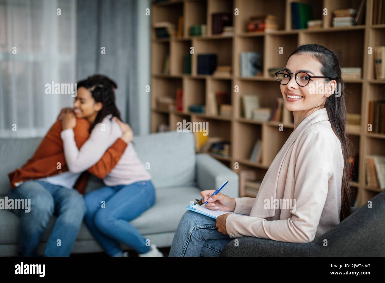 Glad young caucasian male hugging black female at meeting with doctor